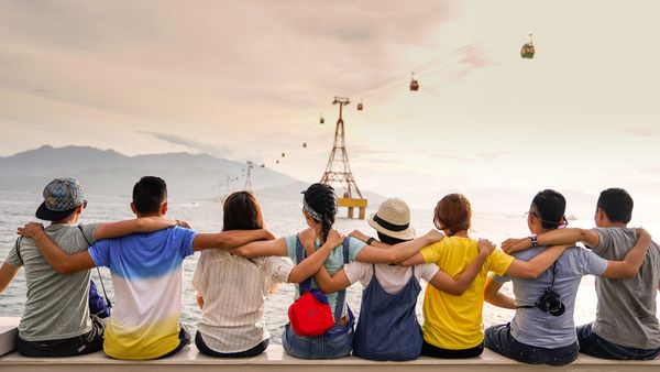 seven friends sitting together facing away from the camera and looking at the ocean and distant hills