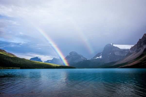 a double rainbow over lake surrounded by snow-capped peaks