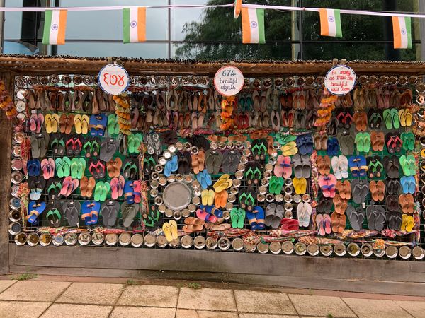 pairs of colourful slippers and shiny trinkets put up on a vertical display stand under a string of Indian flag pennants
