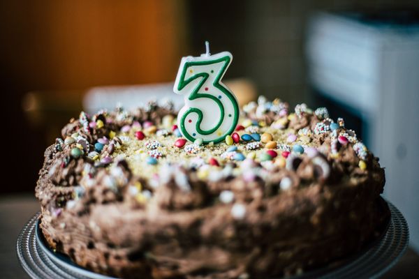 chocolate cake topped with sprinkles and a candle in the shape of the number three