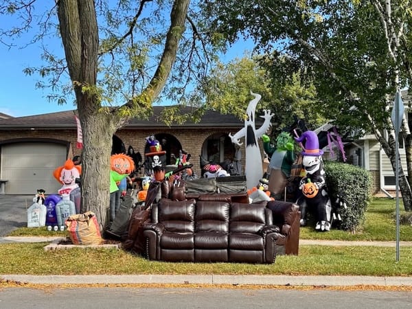 a three-seater brown leather sofa abandoned on the sidewalk surrounded by Halloween inflatable monsters