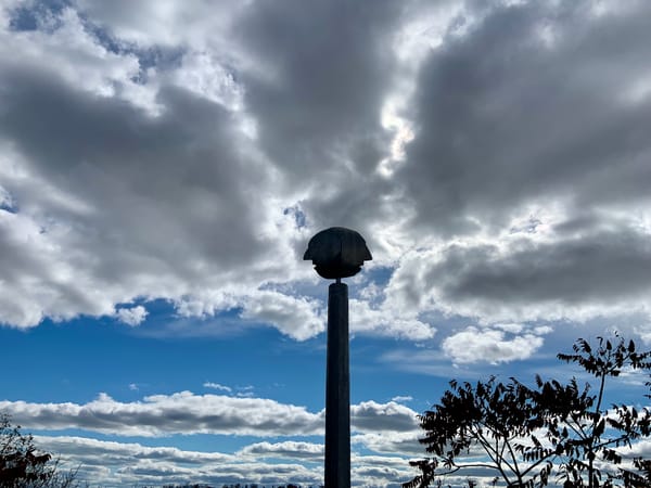 silhouette of a metal sculpture featuring a pole atop which is a two-faced head with the two faces looking out in opposite direction