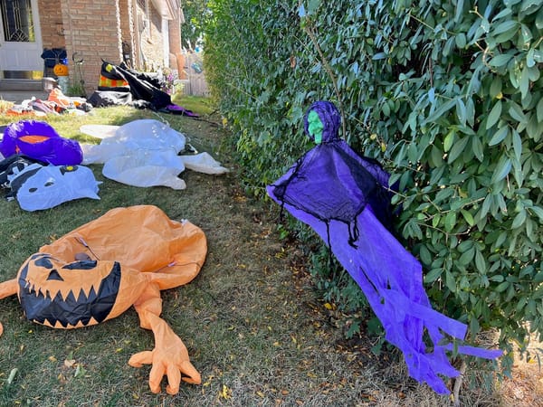 deflated monsters - a witch, a pumpkin, ghosts - scattered on the hedges and the front lawn of a house