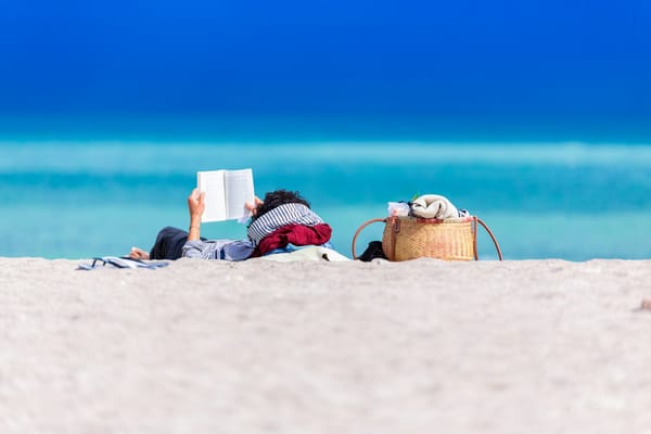 person lying on the beach reading a book against the turquoise blue of the ocean