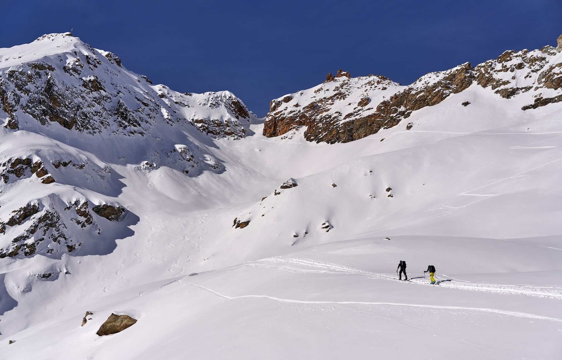 two mountaineers walking on a snowy path leading to mountain peaks
