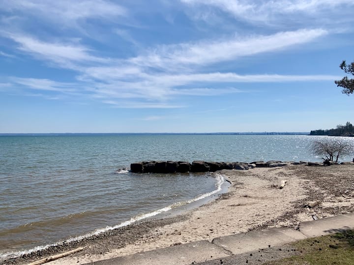 Lake Ontario under a blue sky with a sandy strip and a rocky pier