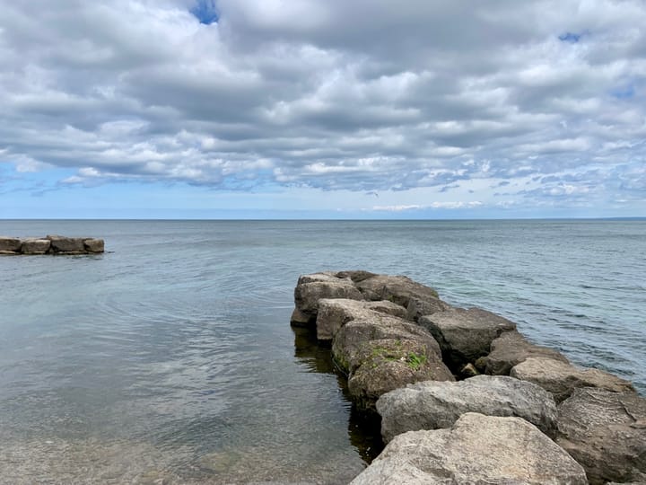 a rocky extension jutting out into Lake Ontario under a blue sky with white clouds