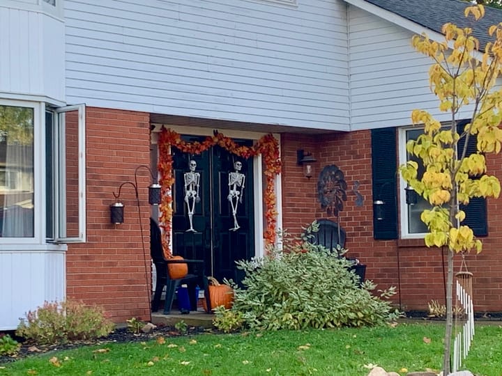 two tiny skeletons hung on the front door of a house with fall leaf decoration and pumpkins